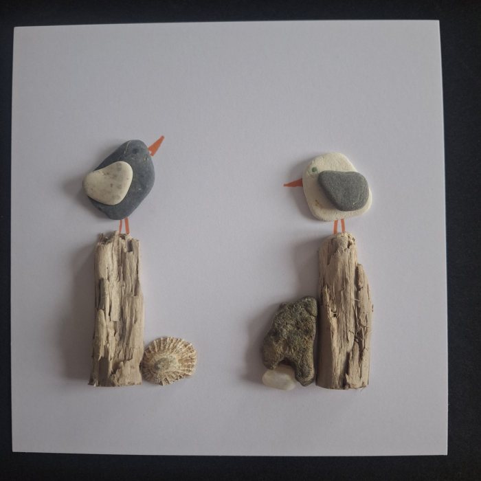 Oystercatcher and Gull: a dark pebble bird and a pale pebble bird on driftwood posts